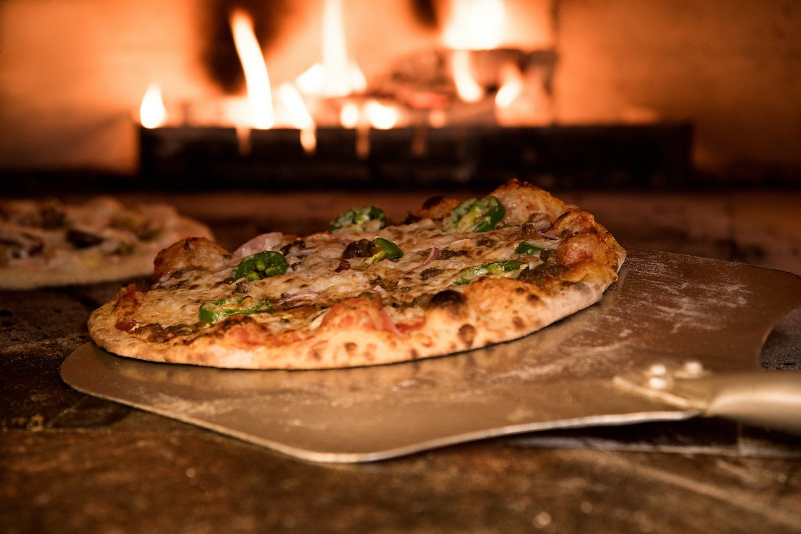 Freshly baked pizza on a peel in front of a glowing wood fire
